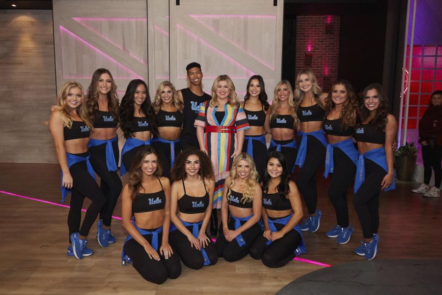 Members of the UCLA Dance Team posed with Kelly Clarkson after performing on her daytime talk show. Dance Team members are wearing black sports bras and black leggings.